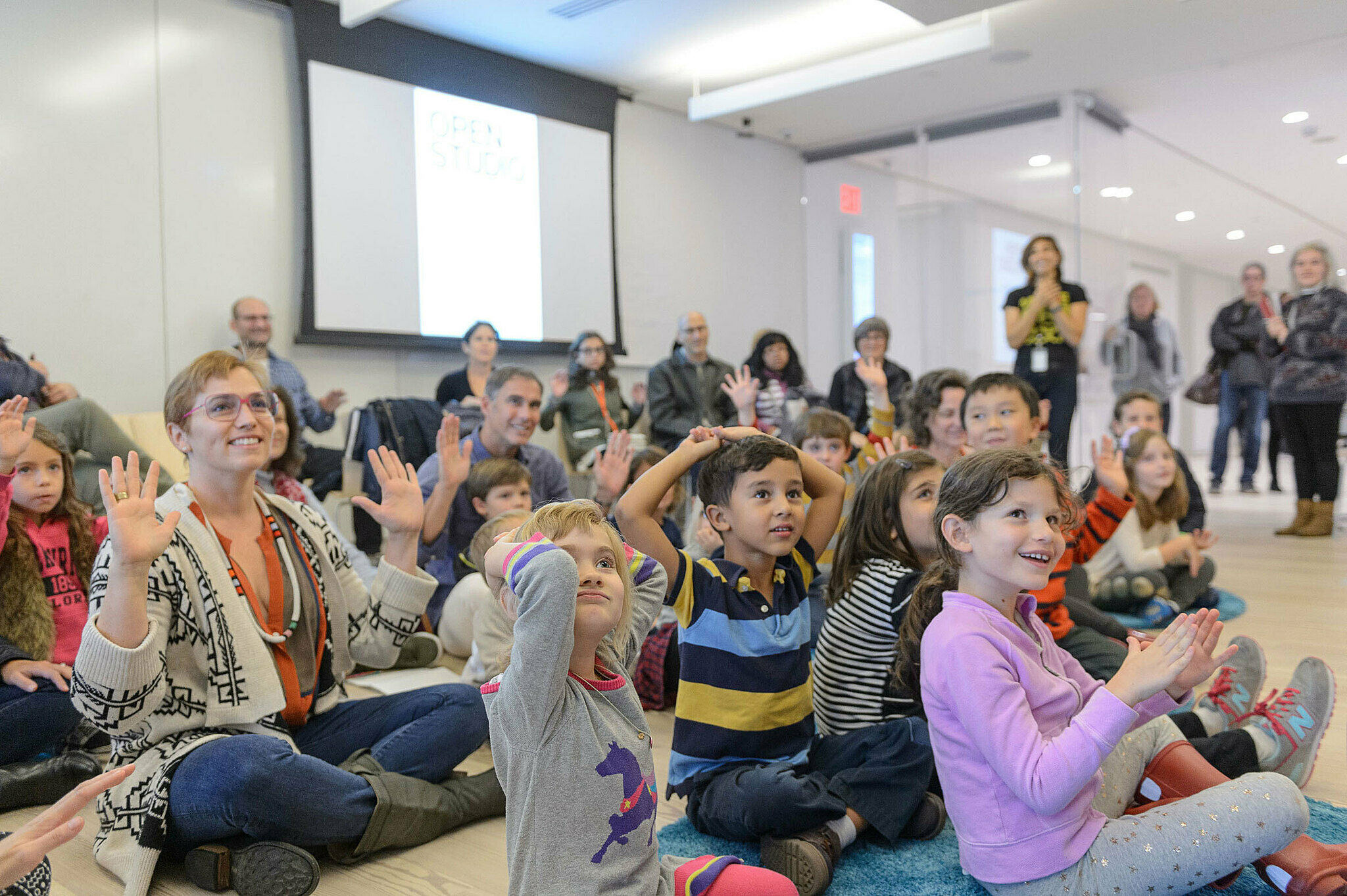 Families raise their hands in an Open Studio workshop led by artist Cooper-Moore.