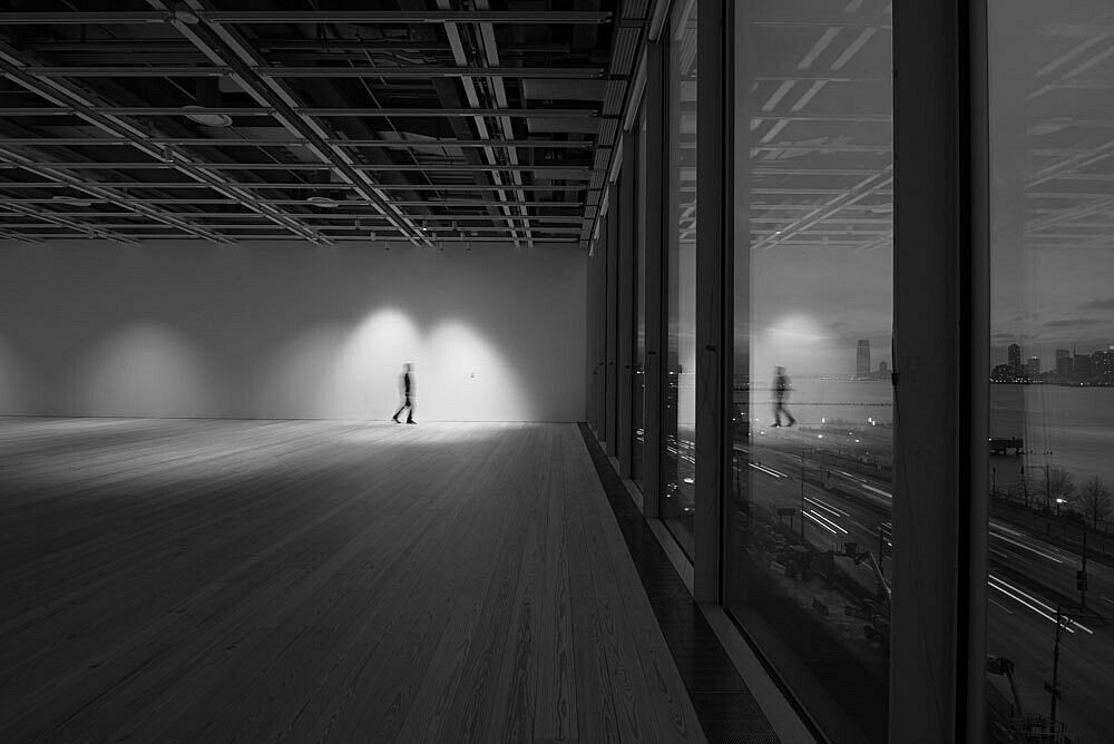 A lone figure stands in the empty fifth floor galleries of the Whitney Museum lit at night