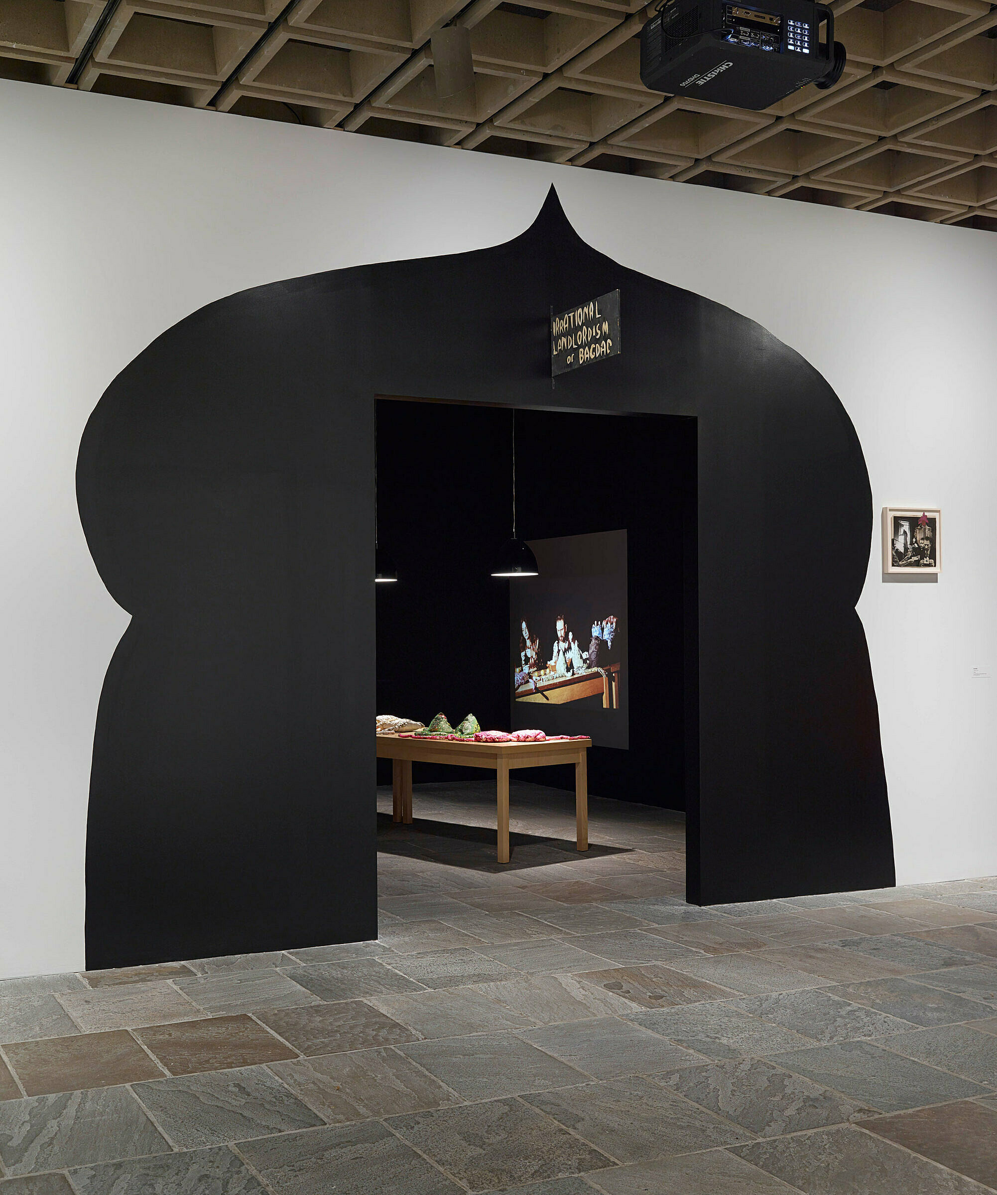 An art installation with a table and video in a gallery.