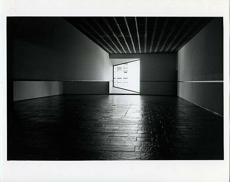 Long view of a darkened gallery with a window at the end of the room.
