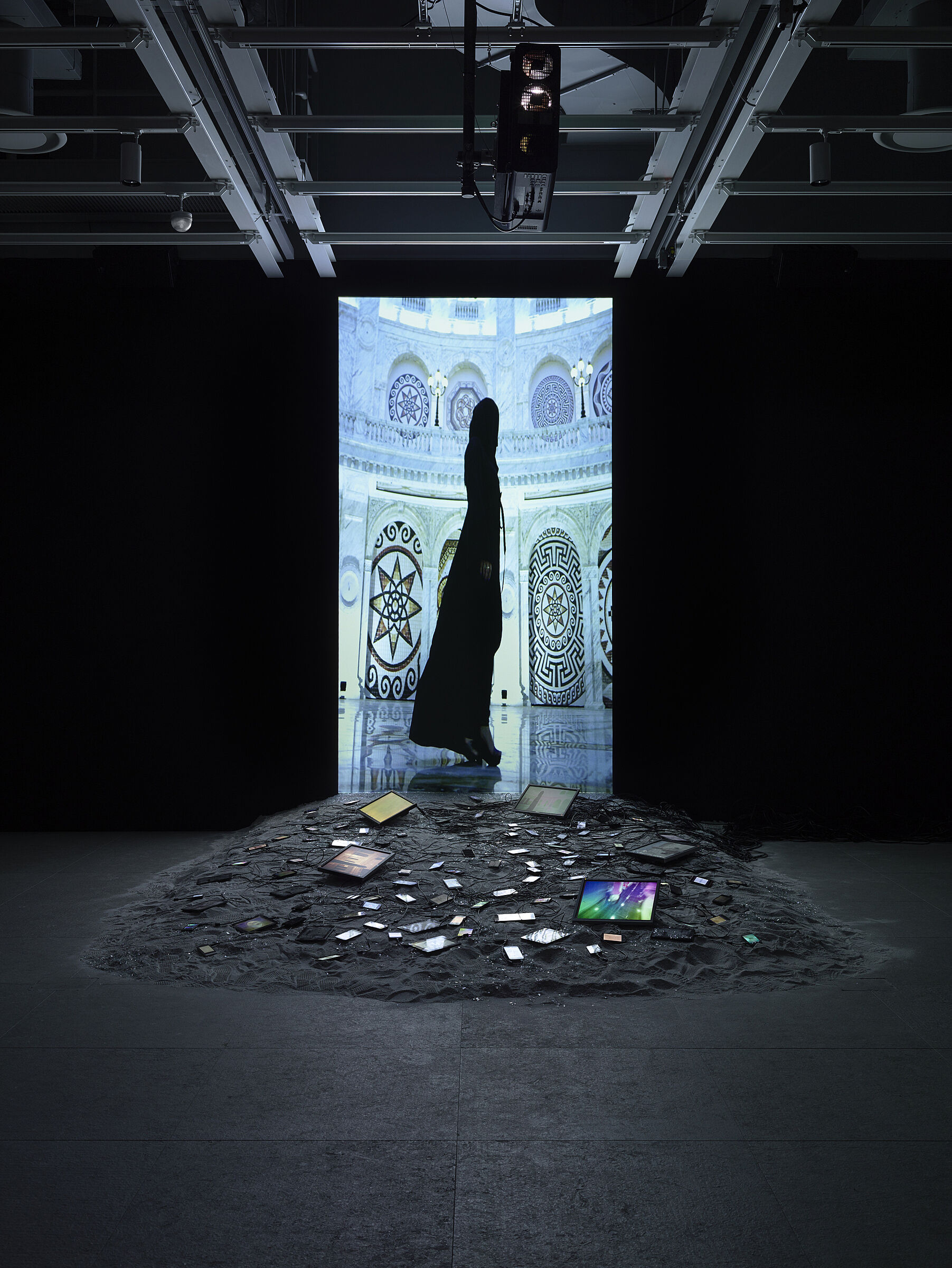 Video installation by Sophia Al-Maria with a black image of a woman standing on screen.