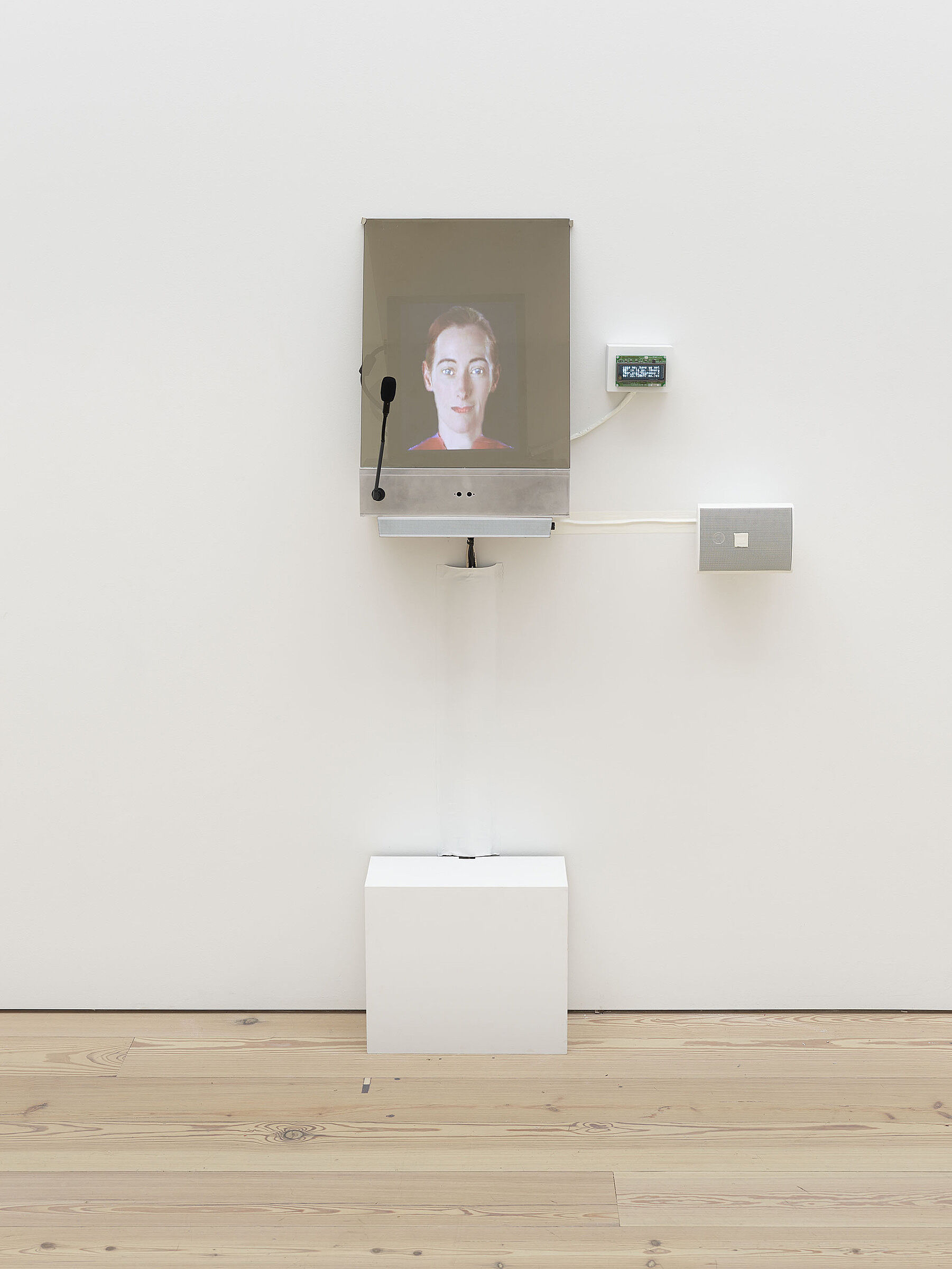 A small video screen on a gallery wall projecting a person's face.
