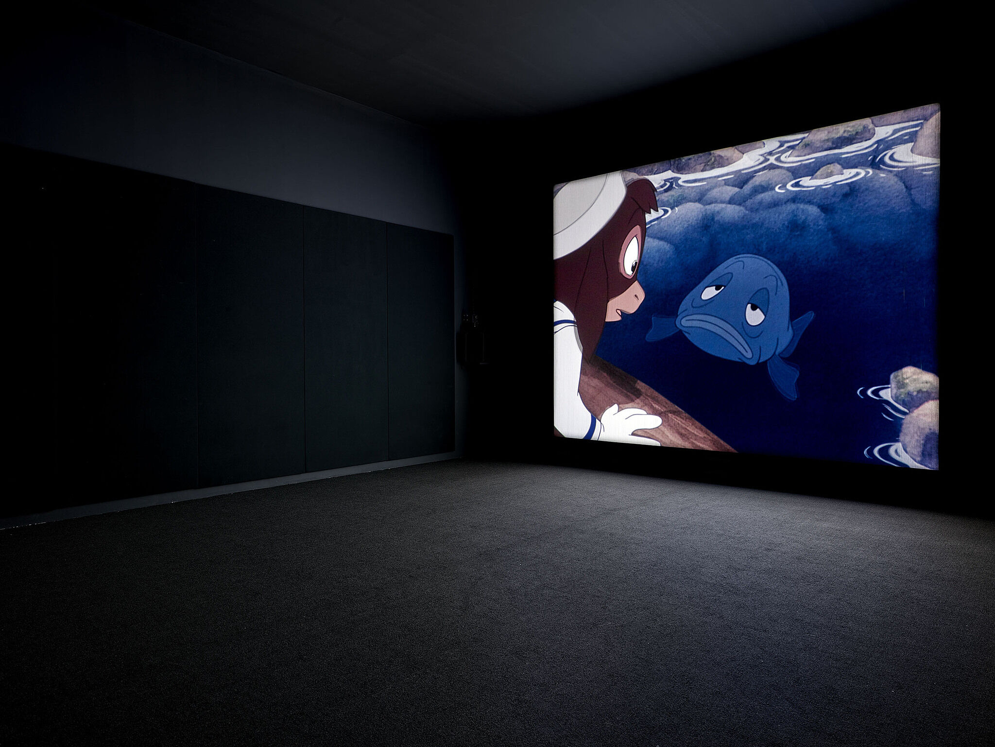 A video screen shows a fish and animals on the wall of a gallery.