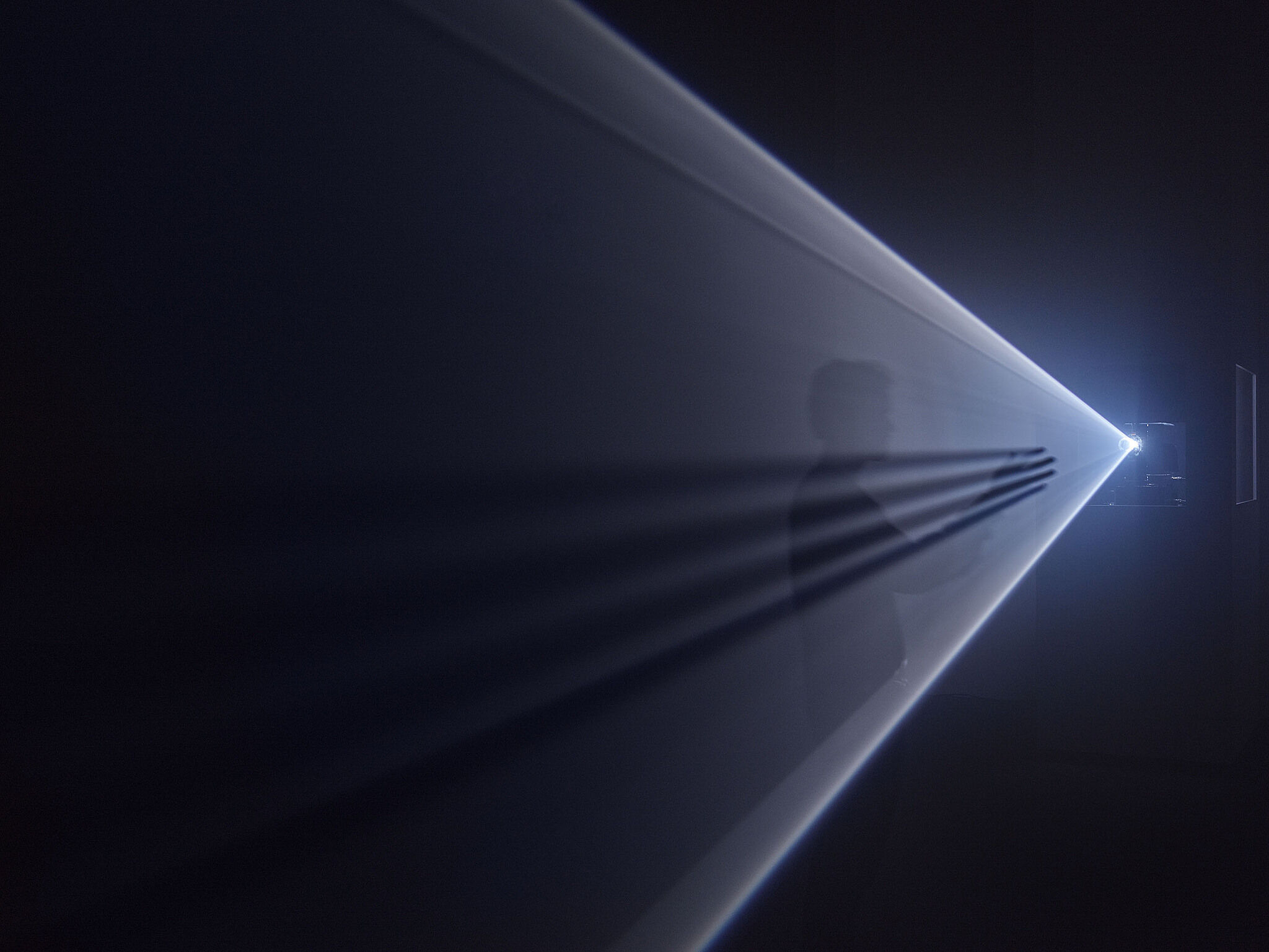 A person stands in the middle of a beam of light from a projector. 