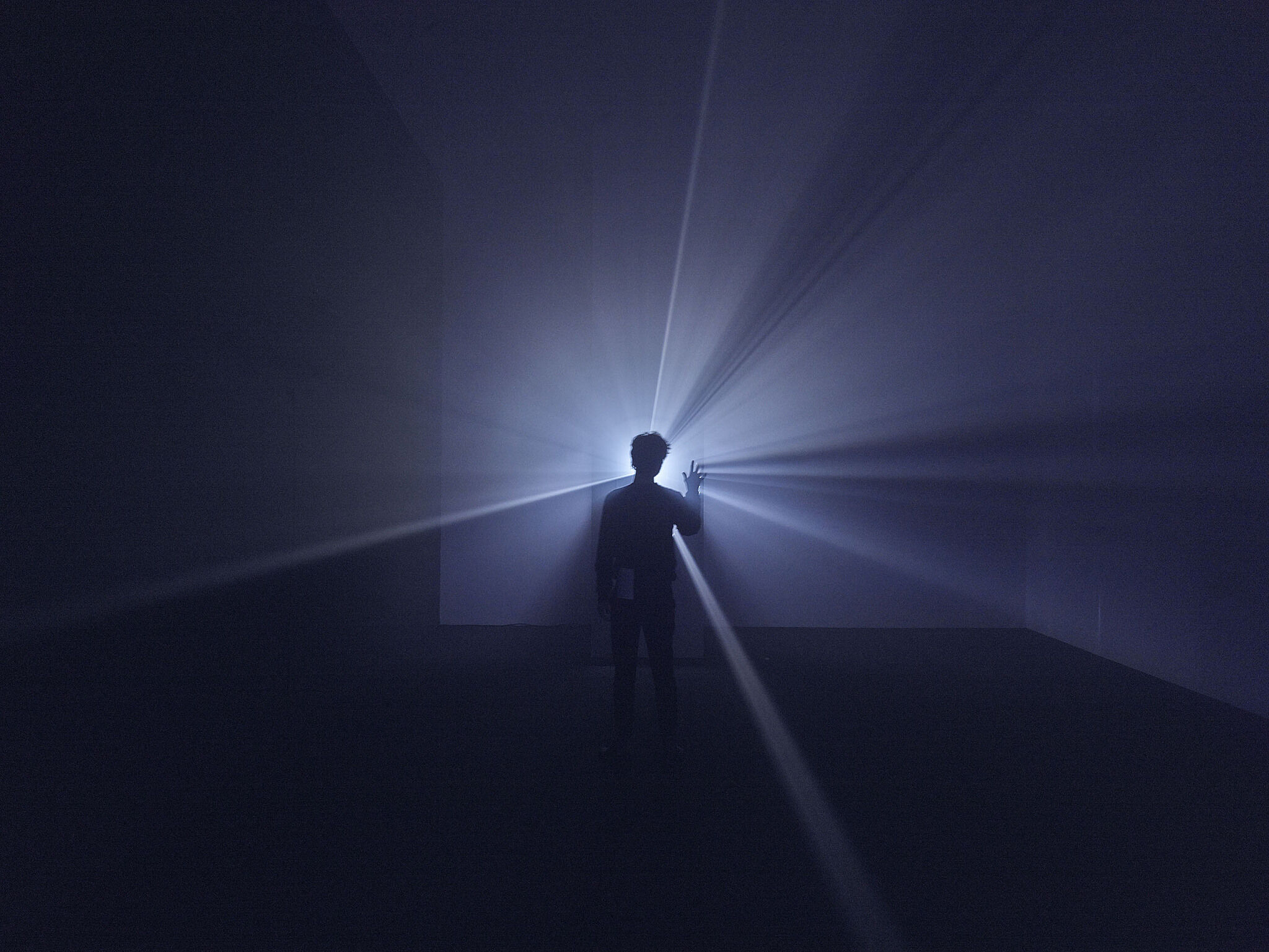 A man stands in front of a film projector diffusing a beam of light.