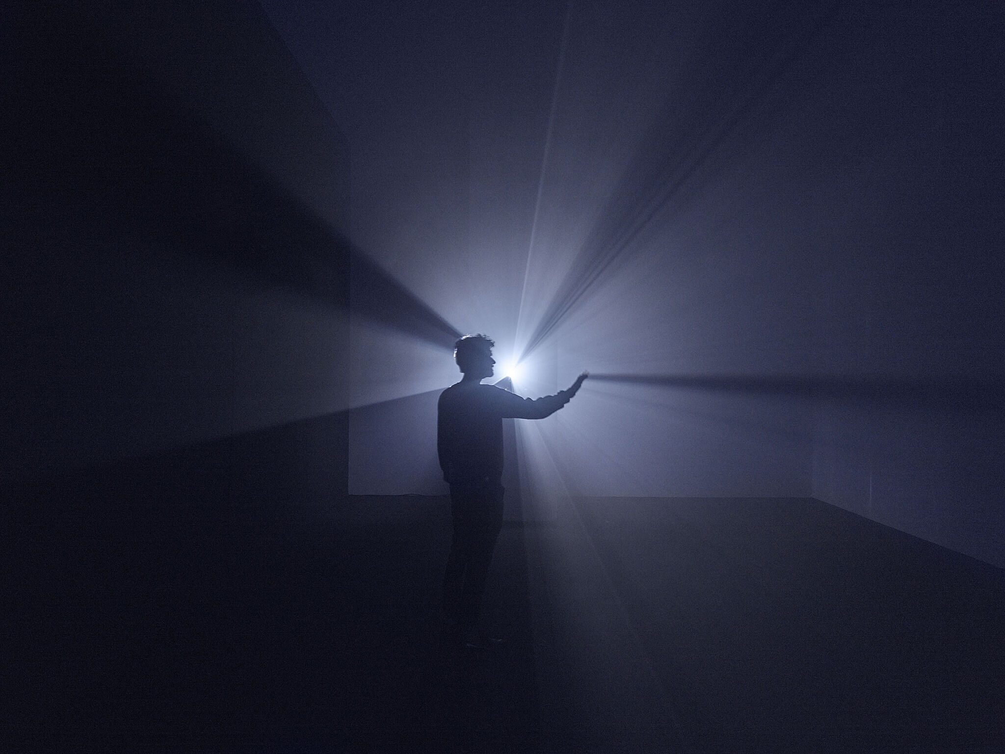 A man stands in front of a projector blocking a beam of light.