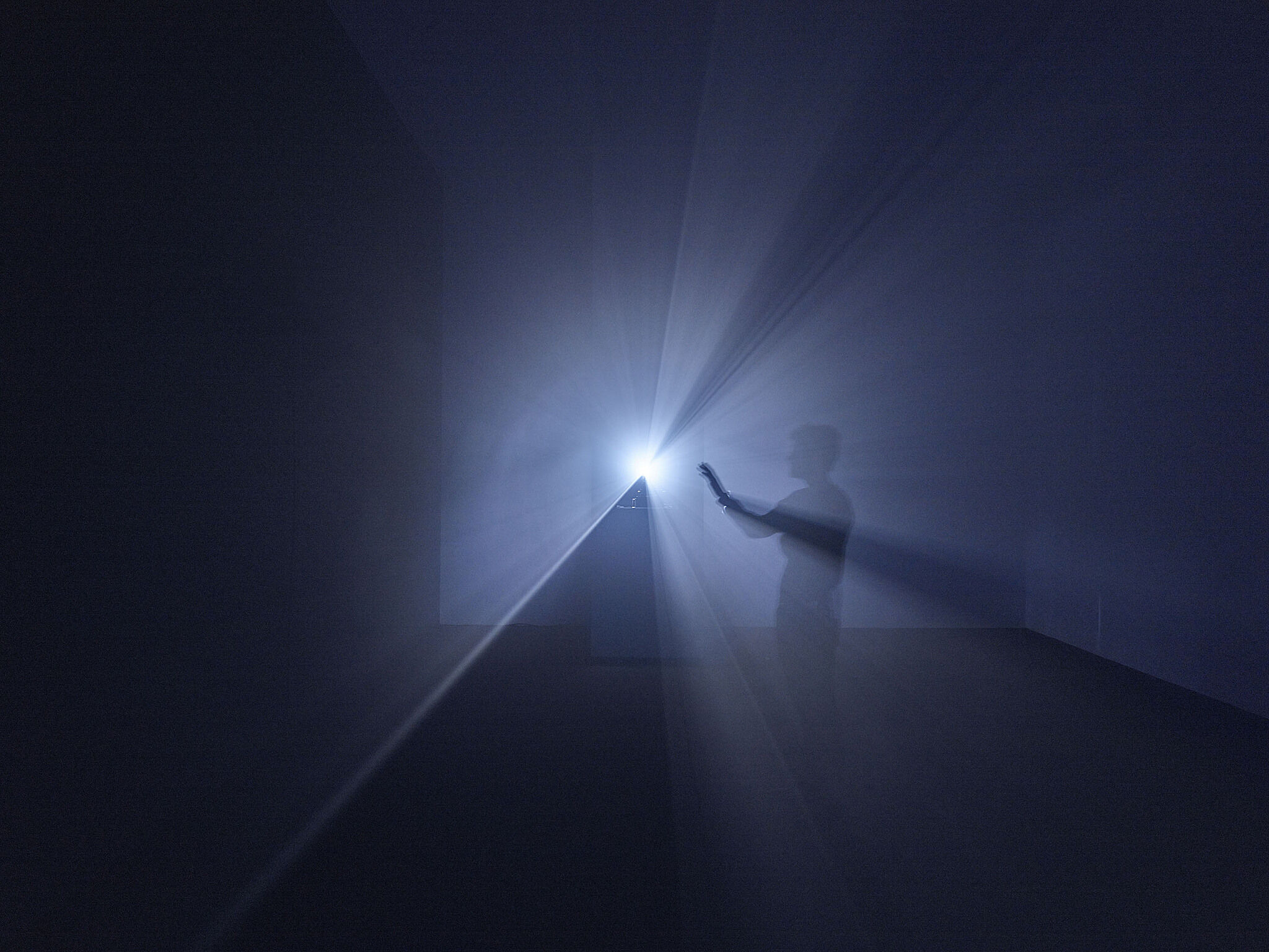 A man holds his hand out towards a beam of light from a film projector.