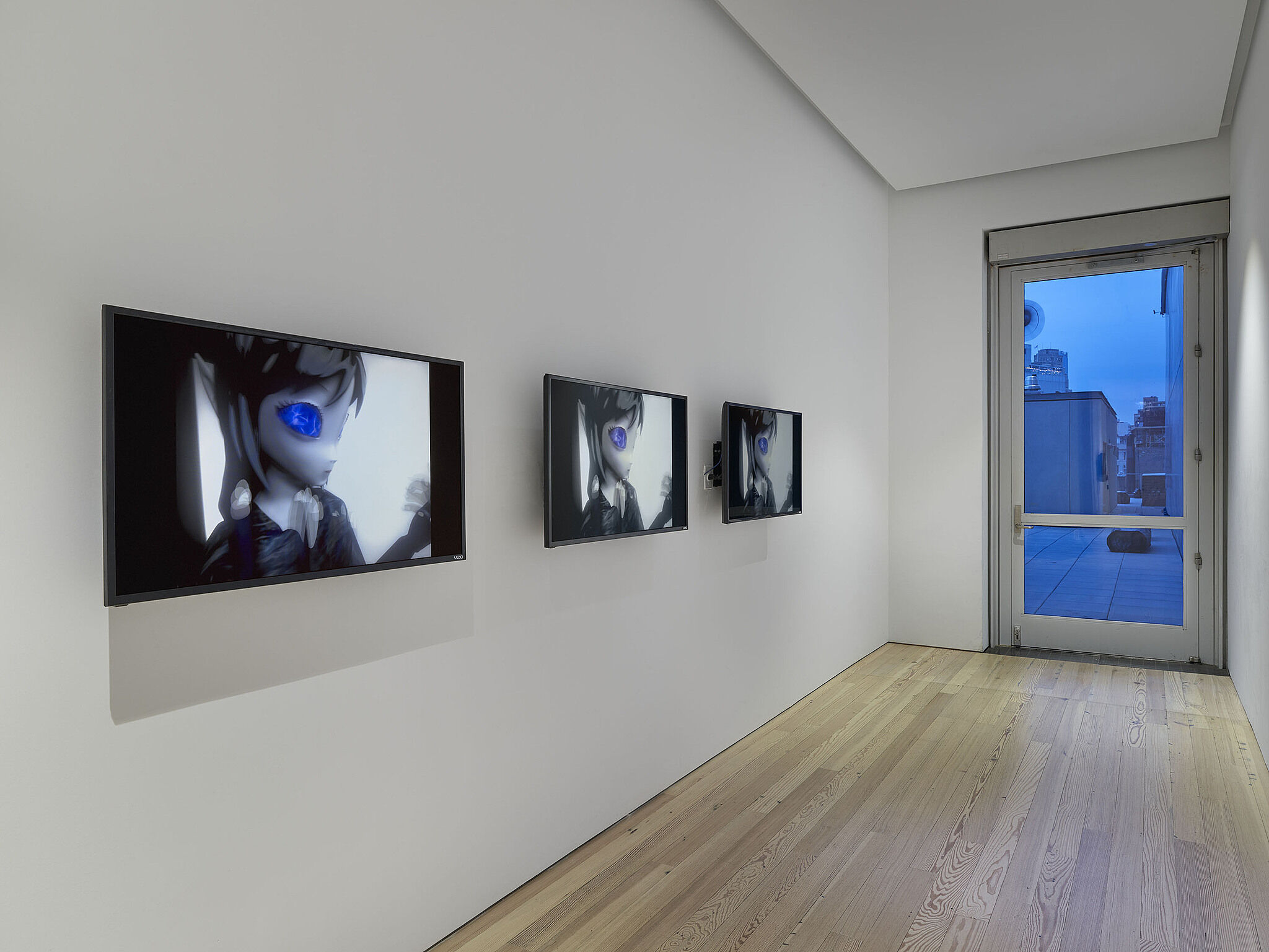 Three screens showing an alien figure on the wall of a gallery with a window.
