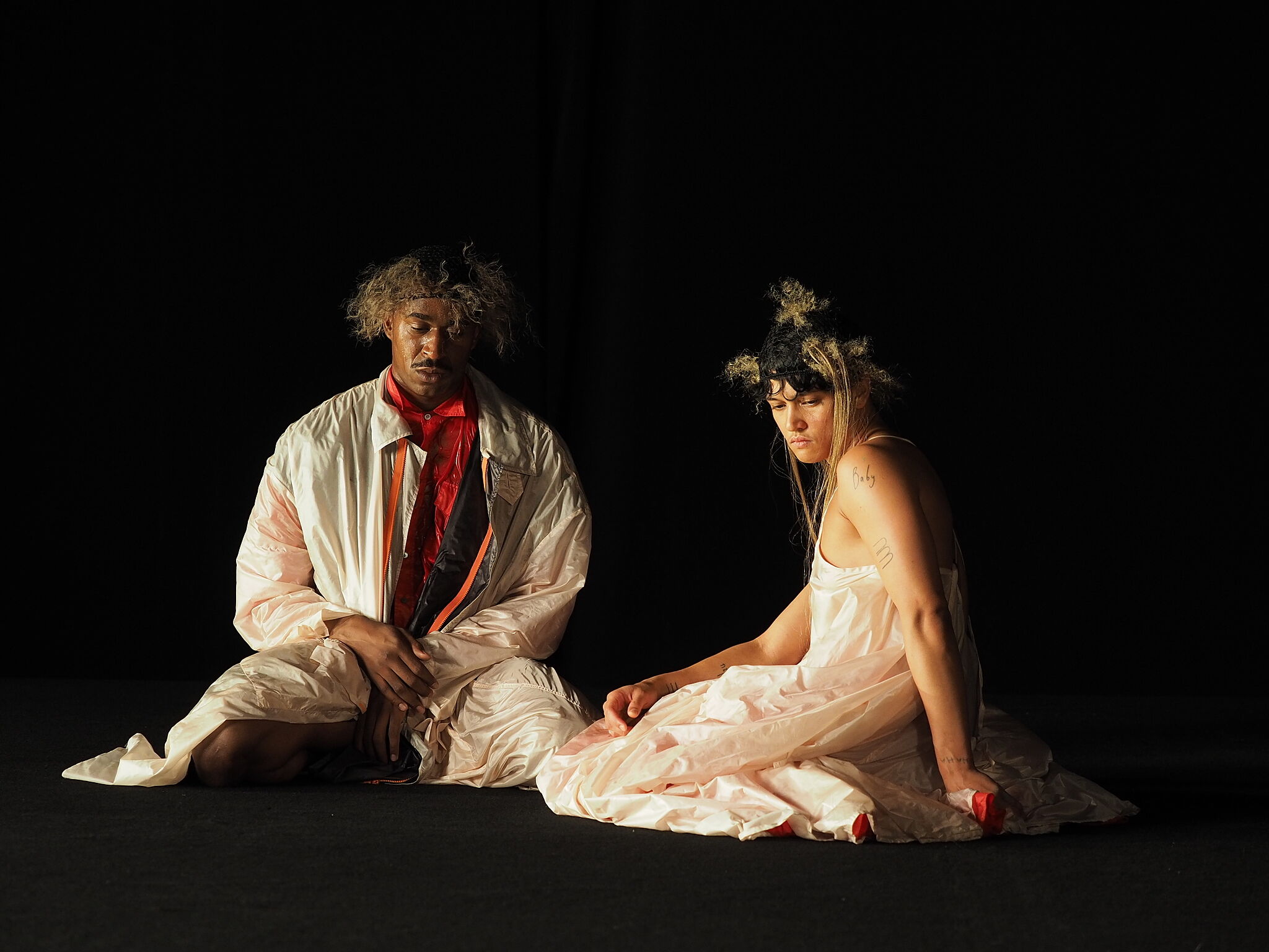 Image of two people sitting on the ground with their eyes downcast