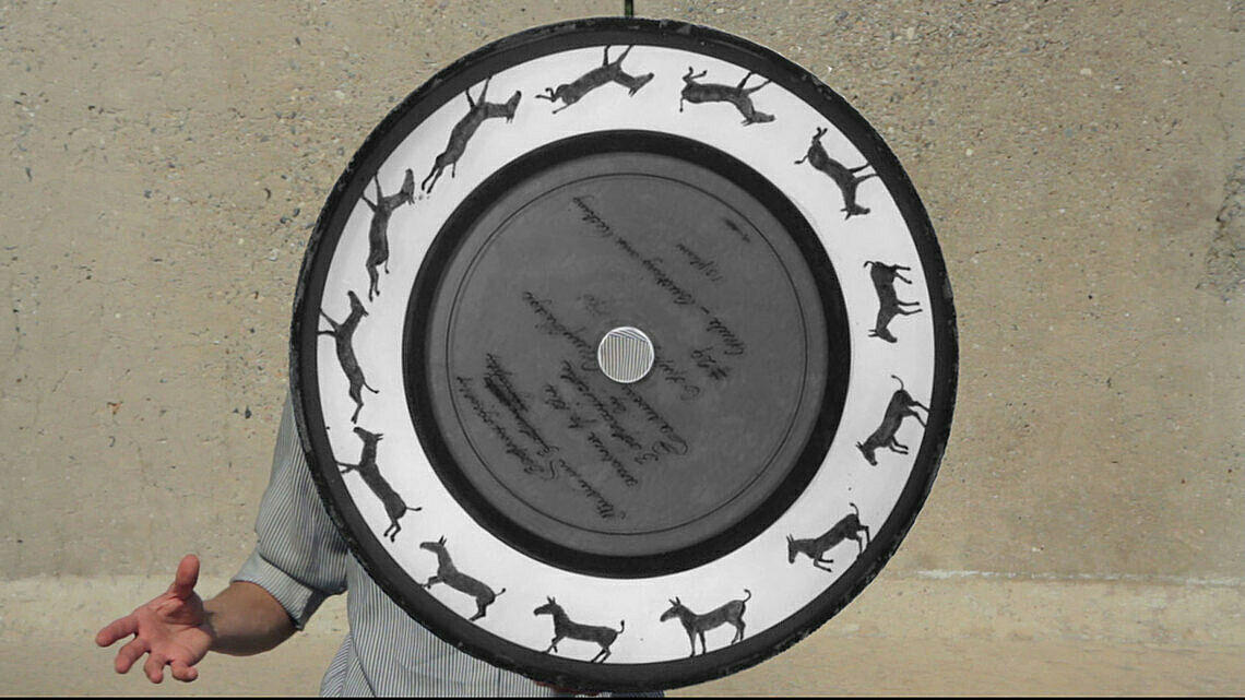 A person holds a large spinning disc showing a sequence of running animal images around the edge.