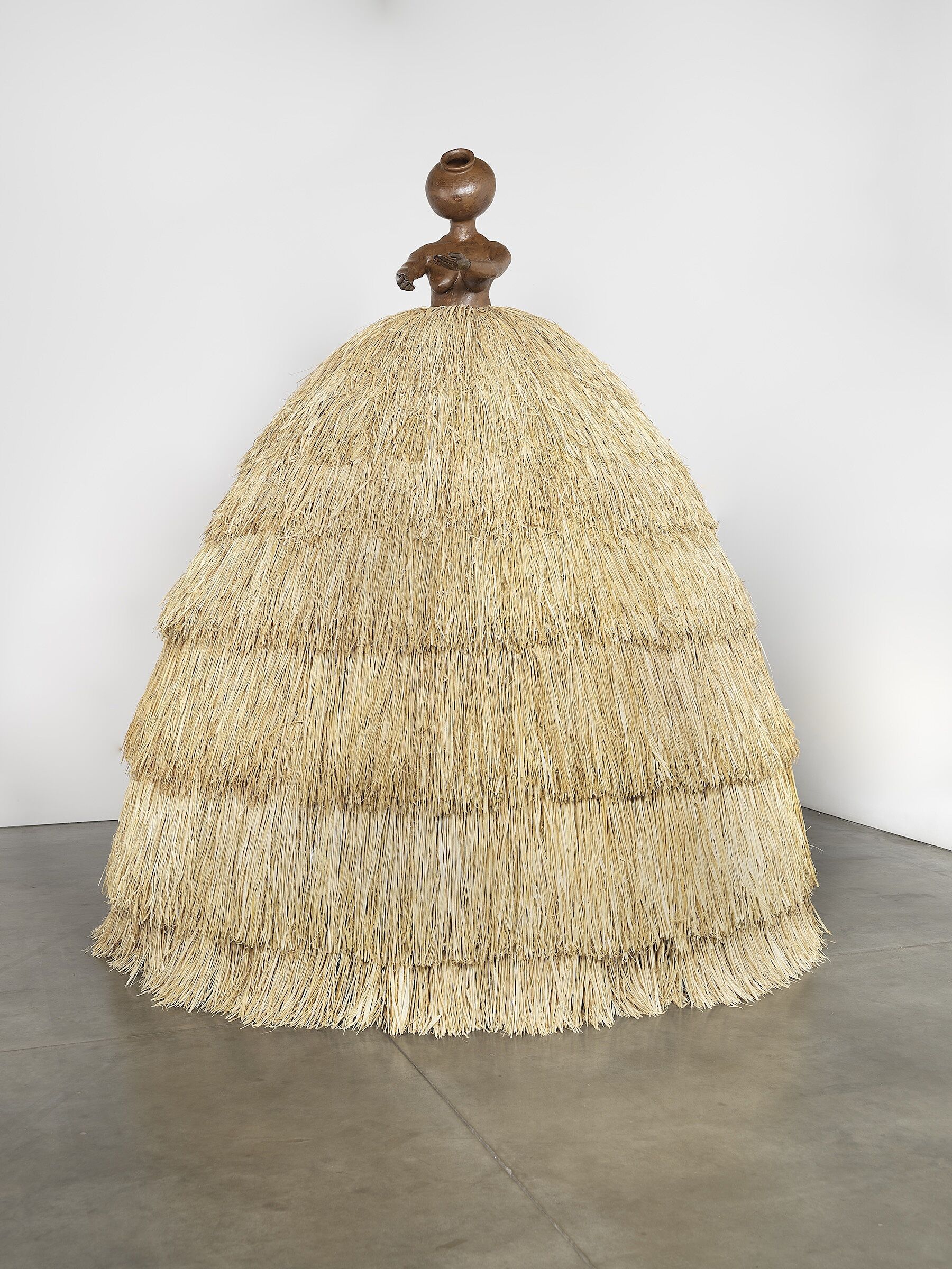 A sculpture of a small stone figure wearing a wide straw-like skirt.