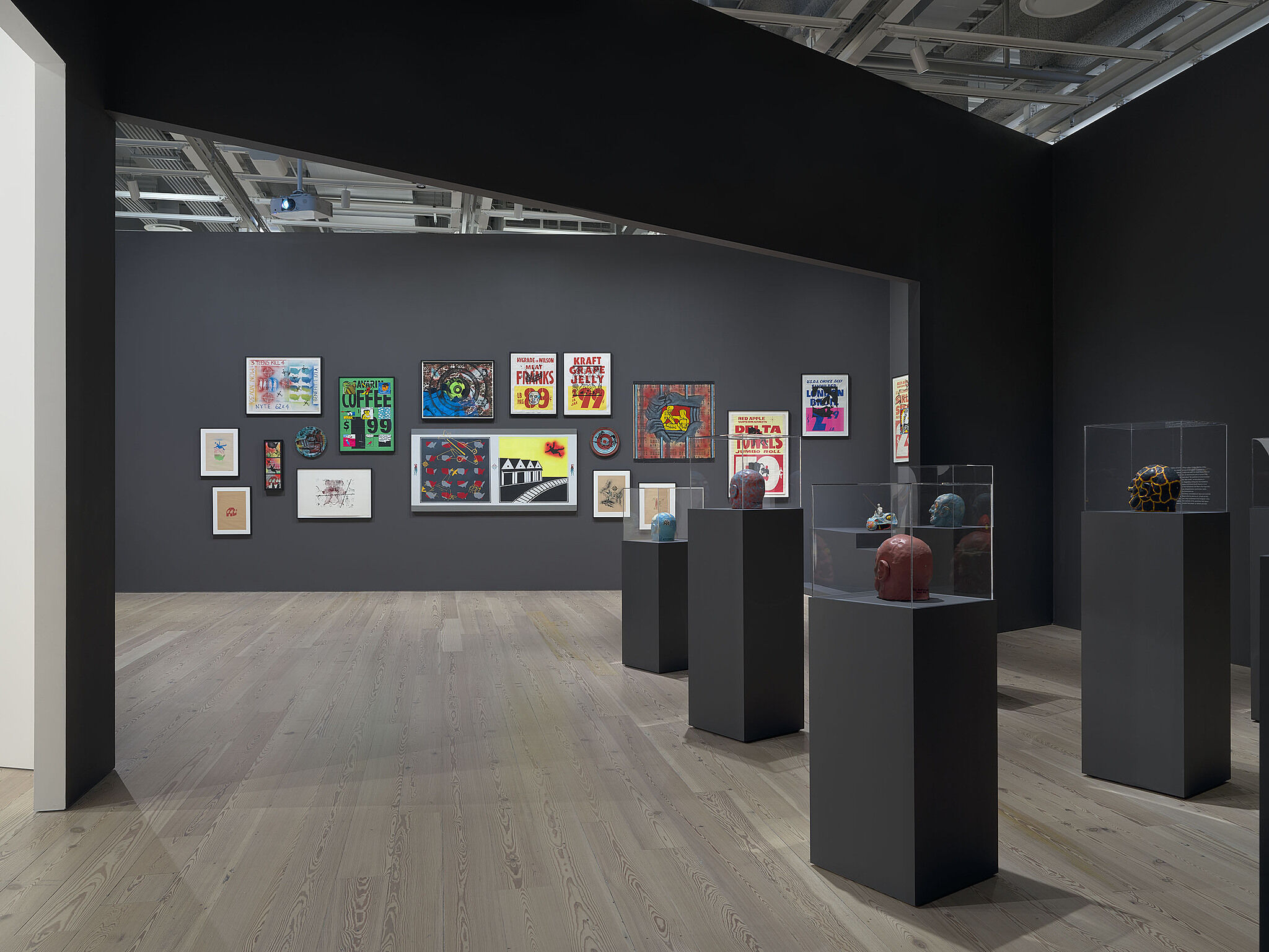 An image of the Whitney galleries with paintings on the wall and standing vitrines