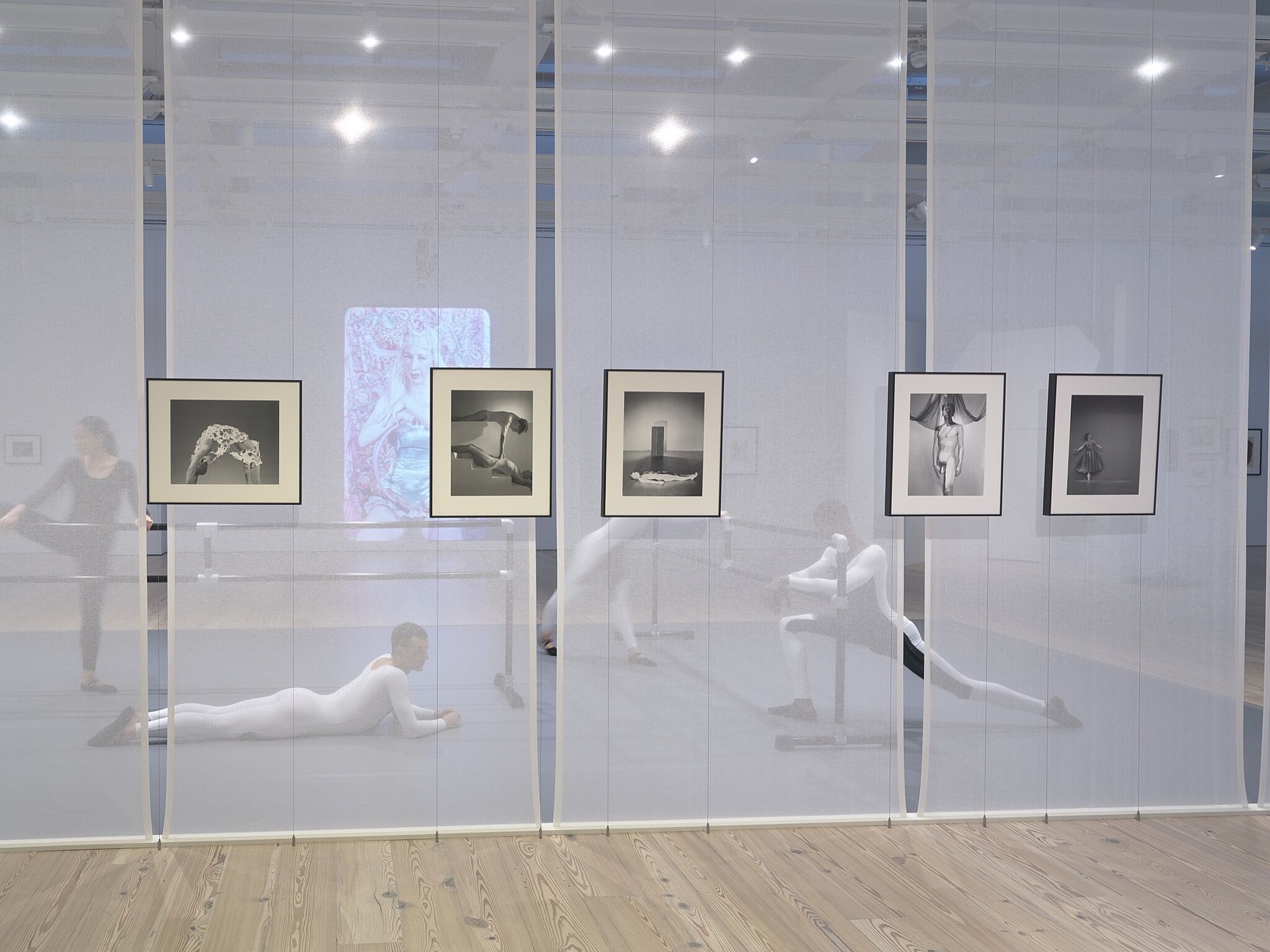 A group of dancers stretching in a gallery with photos on the walls.