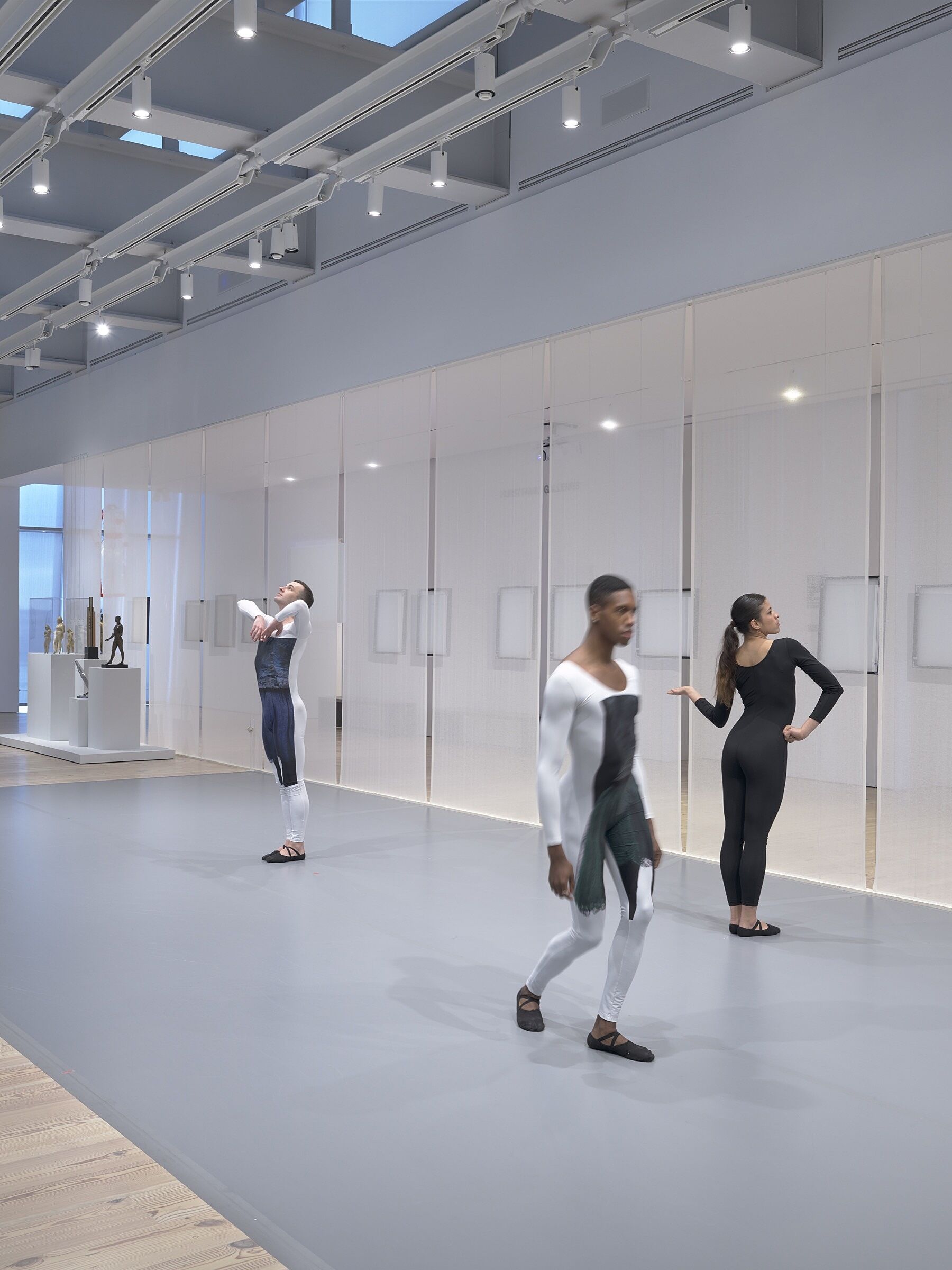 Three dancers perform in a gallery space full of photos and sculptures.