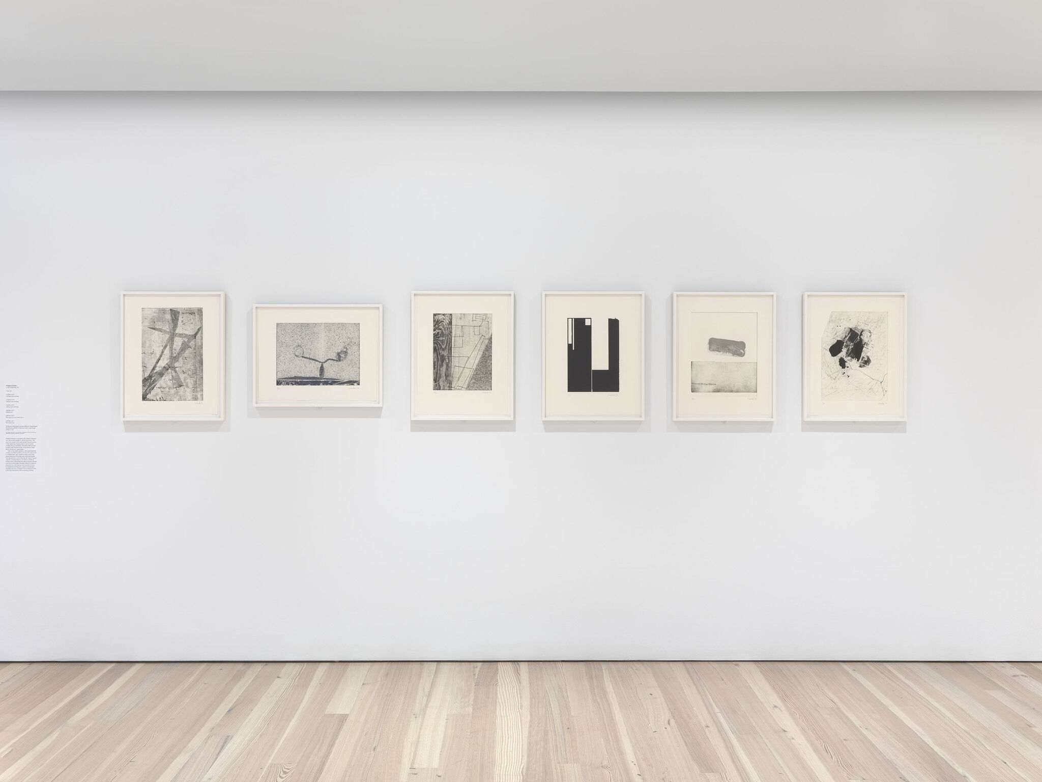 Six works of art displayed in a row on a white wall.